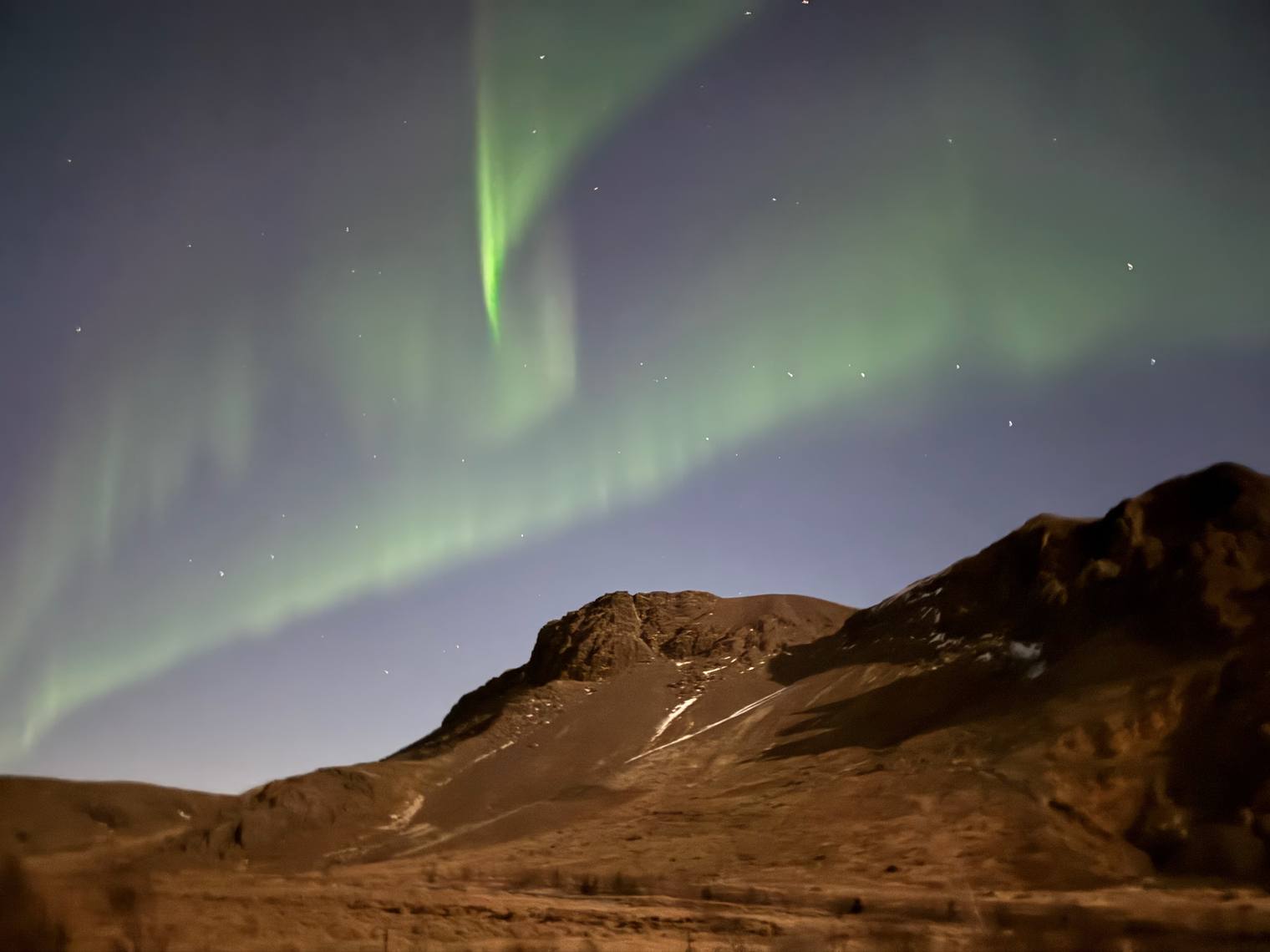 Green northern lights over a brown hillside under a starry sky