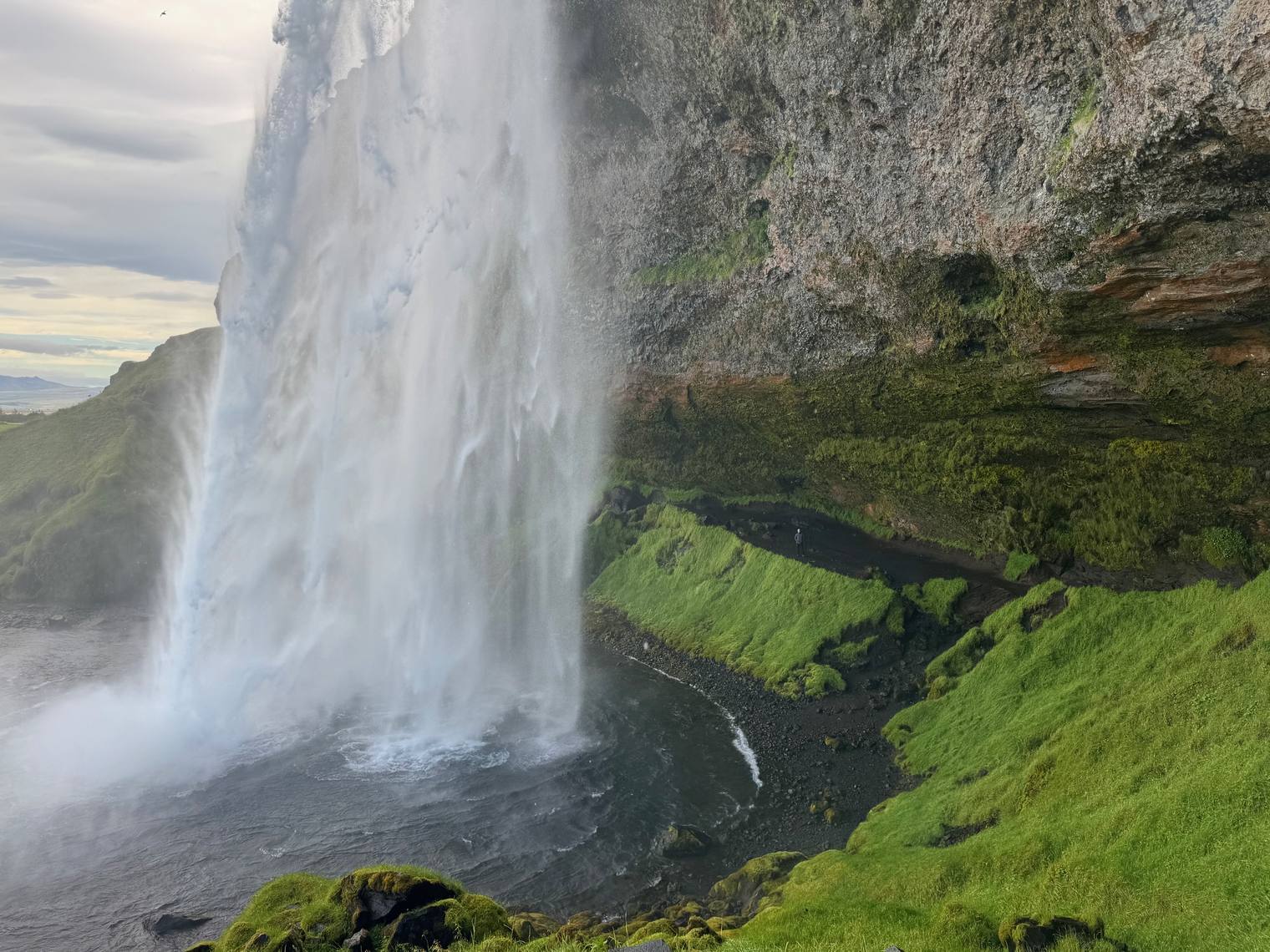 Seen from behind, a tall waterfall falls beside a mossy cliff